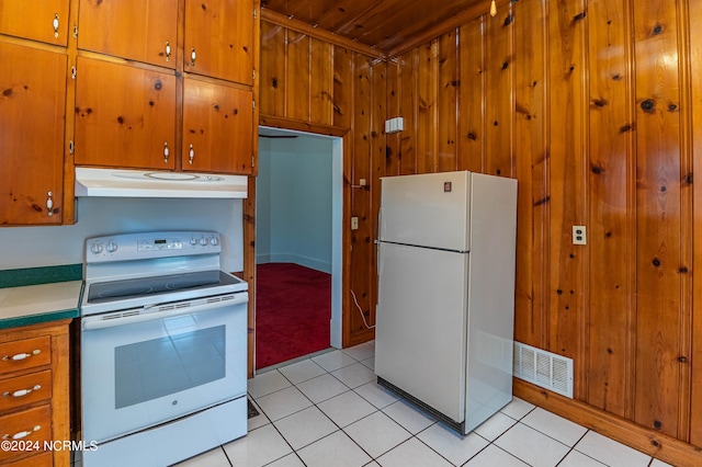 kitchen featuring wooden walls, white appliances, and light tile patterned floors