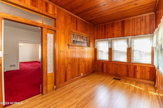 empty room with light wood-type flooring, crown molding, wood ceiling, and wood walls