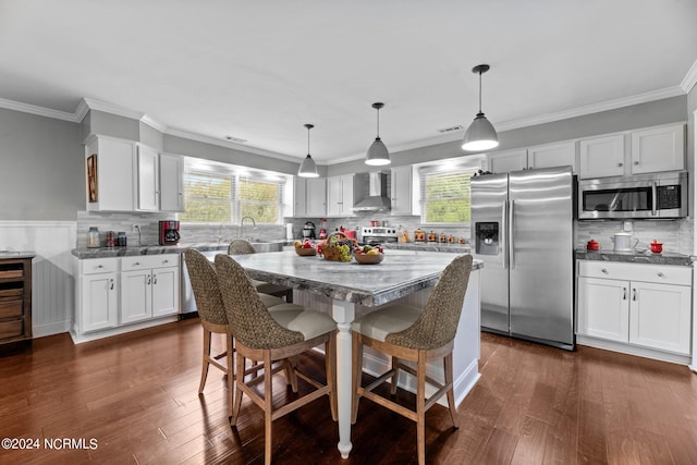 kitchen featuring decorative light fixtures, dark wood-type flooring, wall chimney range hood, stainless steel appliances, and a breakfast bar area