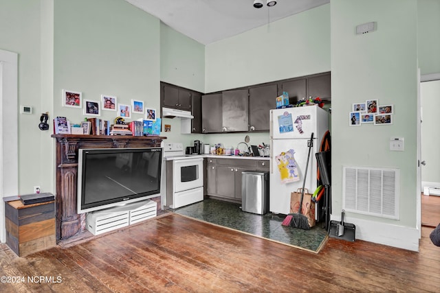 kitchen with a towering ceiling, white appliances, dark hardwood / wood-style flooring, dark brown cabinets, and sink