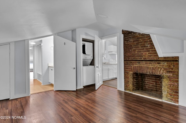 unfurnished living room featuring stacked washing maching and dryer, a fireplace, lofted ceiling, dark hardwood / wood-style floors, and sink