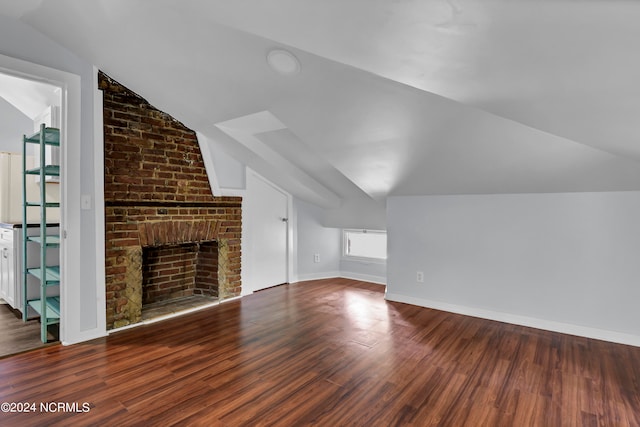 unfurnished living room featuring a brick fireplace, vaulted ceiling, and dark wood-type flooring