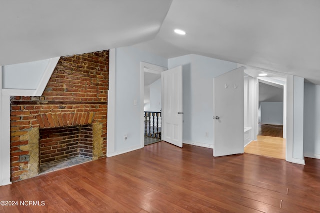 unfurnished living room featuring lofted ceiling, a brick fireplace, and hardwood / wood-style flooring