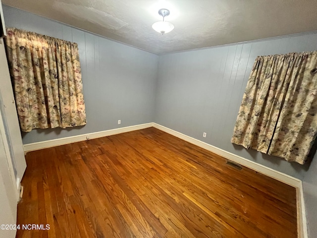 empty room featuring wood finished floors, visible vents, and baseboards