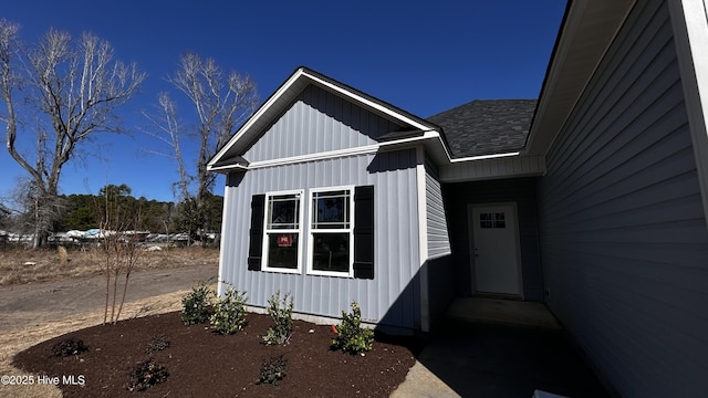 view of exterior entry with board and batten siding and roof with shingles