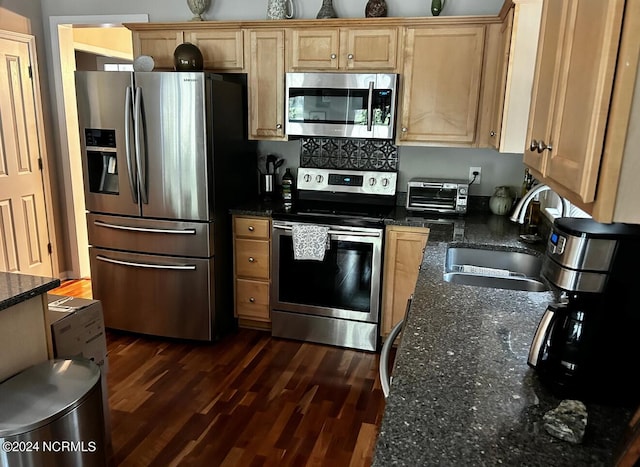 kitchen with appliances with stainless steel finishes, dark stone countertops, dark hardwood / wood-style flooring, and sink