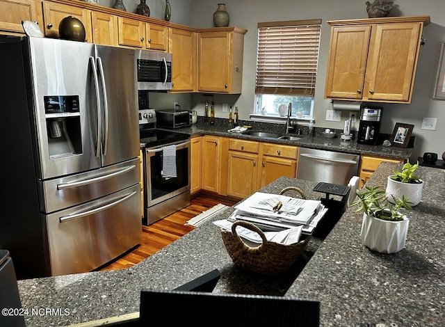 kitchen with dark stone countertops, hardwood / wood-style flooring, appliances with stainless steel finishes, and sink