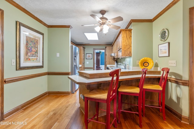 dining room featuring a textured ceiling, crown molding, ceiling fan, and light hardwood / wood-style flooring