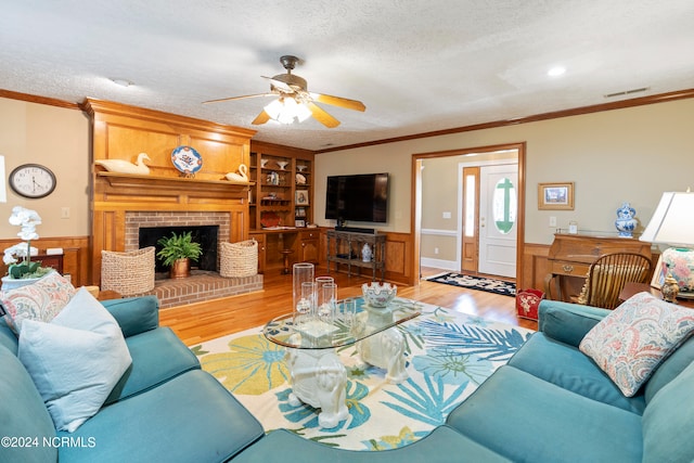 living room with a brick fireplace, light wood-type flooring, ceiling fan, and crown molding