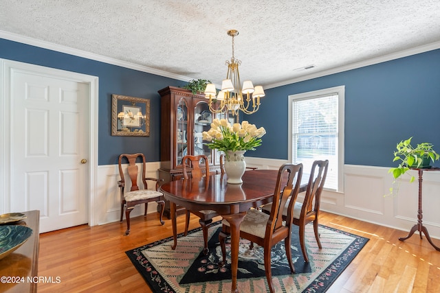 dining space with a notable chandelier, a textured ceiling, crown molding, and light hardwood / wood-style floors