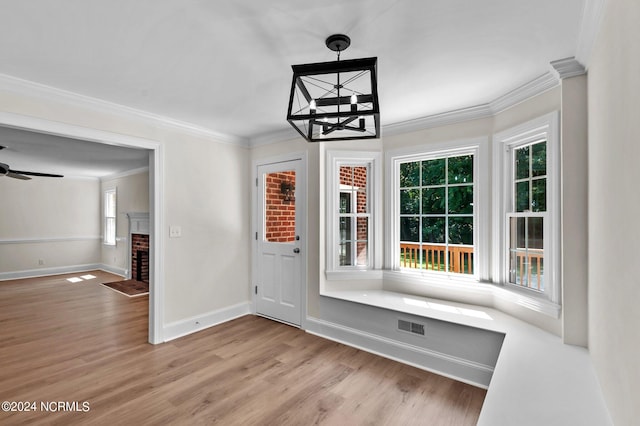 interior space featuring a brick fireplace, ceiling fan with notable chandelier, light hardwood / wood-style flooring, and ornamental molding