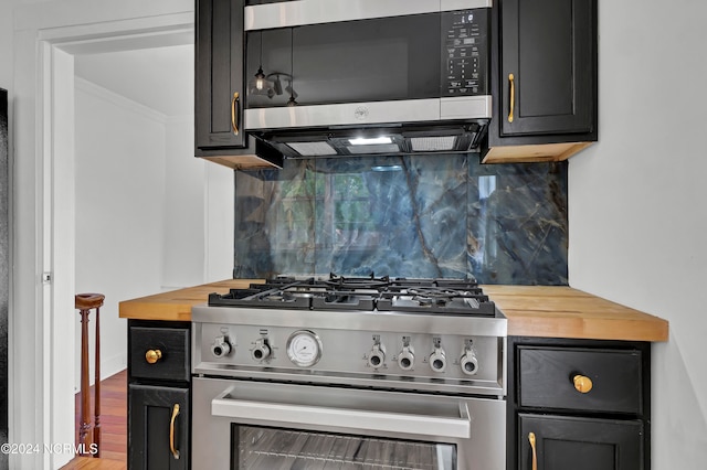 kitchen featuring hardwood / wood-style flooring, appliances with stainless steel finishes, decorative backsplash, and wooden counters