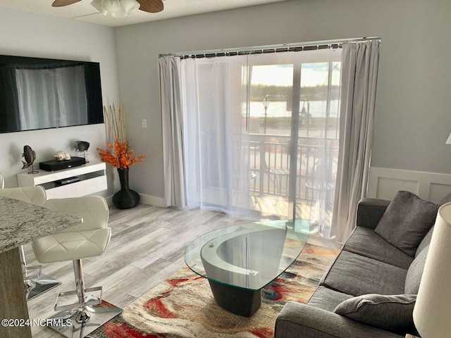 living room with light wood-type flooring, ceiling fan, and a textured ceiling