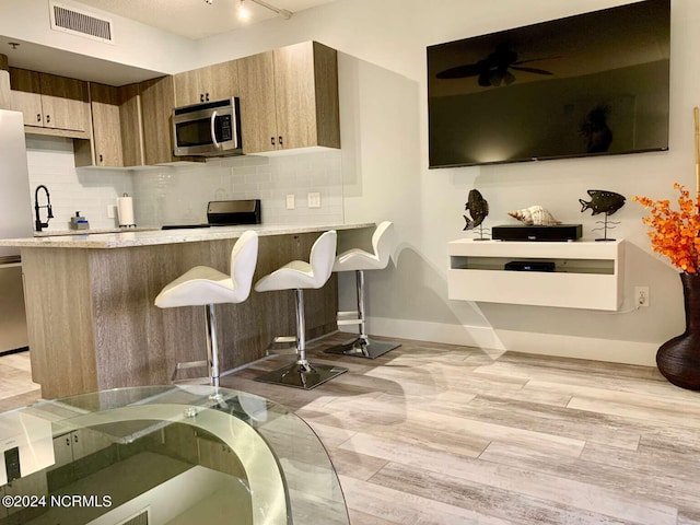 kitchen with light wood-type flooring, decorative backsplash, kitchen peninsula, and a breakfast bar area