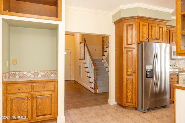 kitchen with decorative backsplash, appliances with stainless steel finishes, light wood-type flooring, ornamental molding, and tile counters