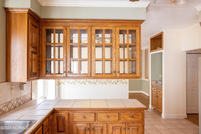 kitchen featuring sink, crown molding, light tile patterned floors, tasteful backsplash, and tile counters