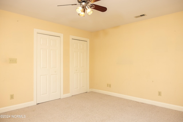 unfurnished bedroom featuring carpet flooring, multiple closets, and ceiling fan