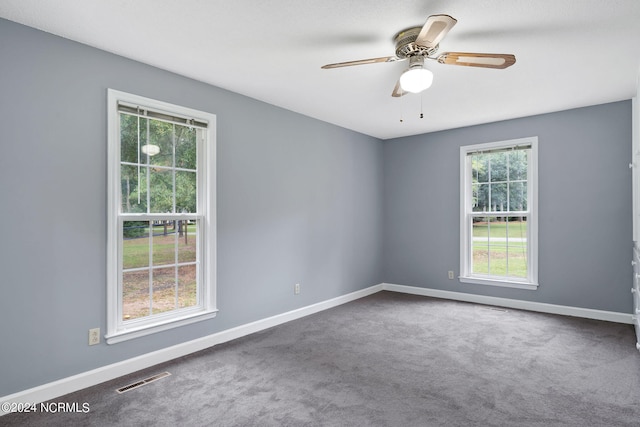 unfurnished room featuring ceiling fan, dark carpet, and a wealth of natural light