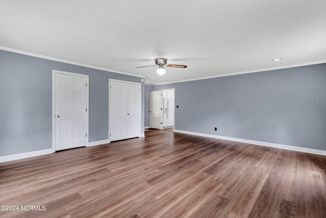 unfurnished bedroom with two closets, ceiling fan, hardwood / wood-style floors, and crown molding