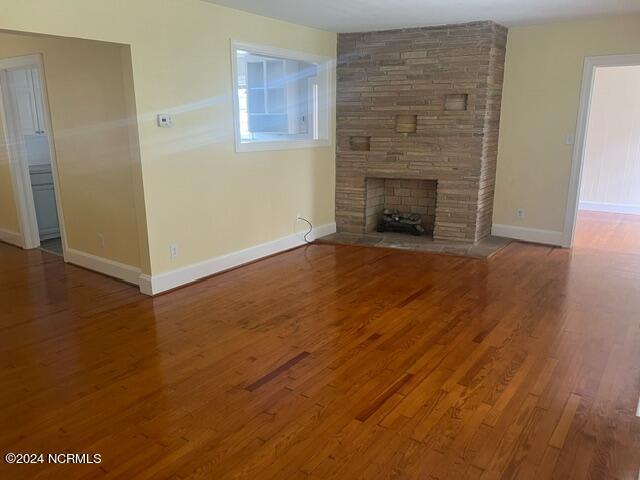unfurnished living room featuring baseboards, a stone fireplace, and wood finished floors
