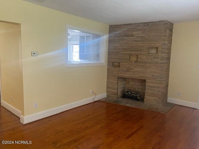 unfurnished living room featuring a stone fireplace, baseboards, and wood finished floors