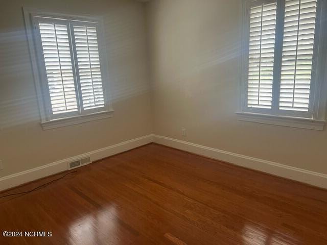 unfurnished room featuring a healthy amount of sunlight, baseboards, wood finished floors, and visible vents
