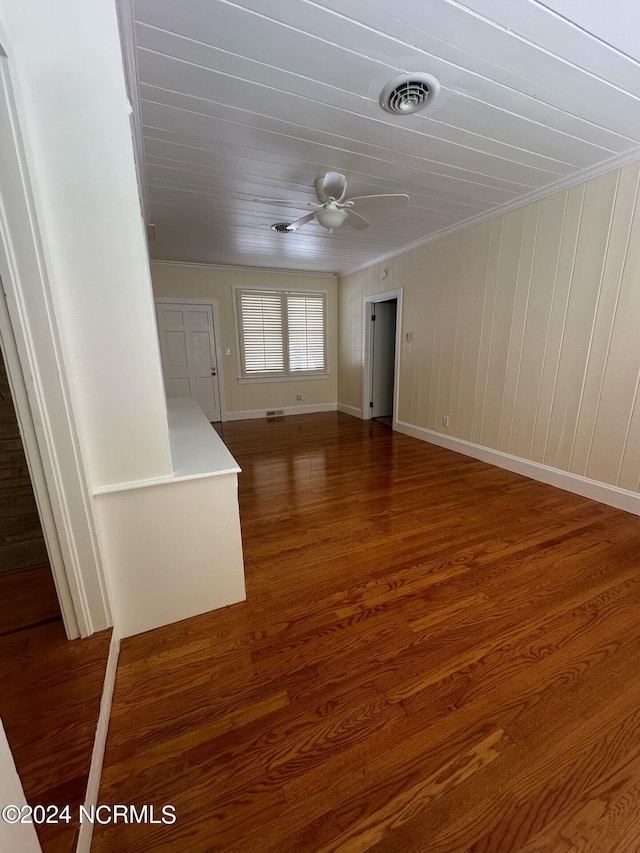 spare room with crown molding, wooden walls, ceiling fan, and dark wood-type flooring