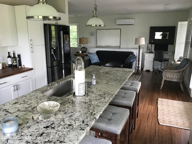 kitchen featuring sink, dark wood-type flooring, black fridge with ice dispenser, light stone countertops, and a wall unit AC