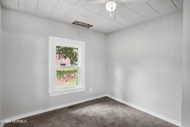 spare room featuring ceiling fan, wood walls, and carpet