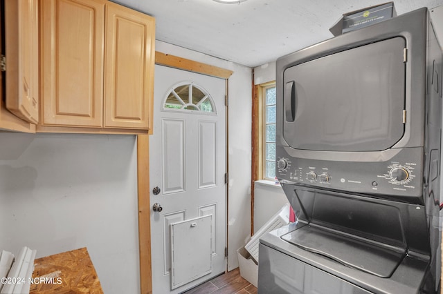 clothes washing area featuring wood-type flooring, stacked washer and dryer, and cabinets