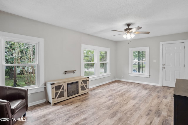 living room with light hardwood / wood-style flooring, a textured ceiling, a healthy amount of sunlight, and ceiling fan