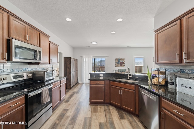 kitchen featuring hardwood / wood-style flooring, tasteful backsplash, sink, stainless steel appliances, and dark stone countertops