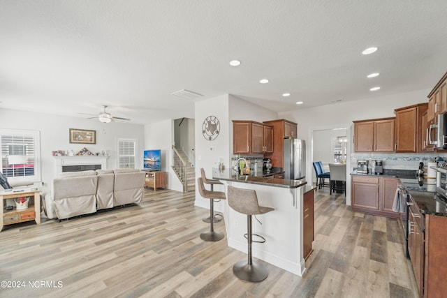 kitchen featuring appliances with stainless steel finishes, decorative backsplash, a kitchen breakfast bar, light wood-type flooring, and ceiling fan