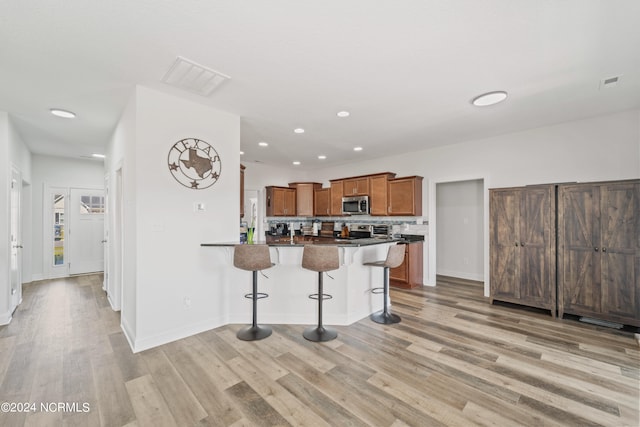 kitchen with a kitchen breakfast bar, stainless steel appliances, light hardwood / wood-style flooring, and tasteful backsplash