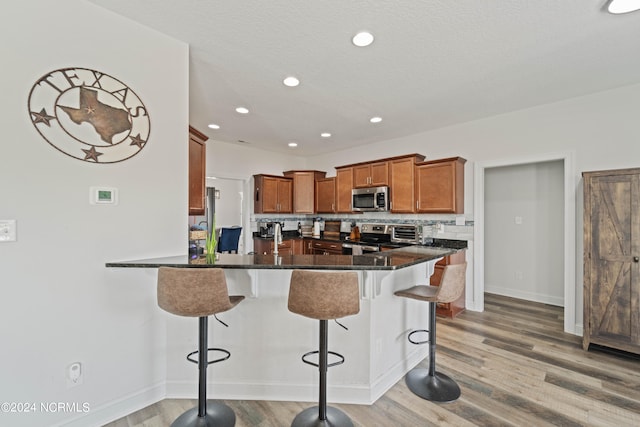 kitchen featuring wood-type flooring, a textured ceiling, a kitchen breakfast bar, decorative backsplash, and appliances with stainless steel finishes