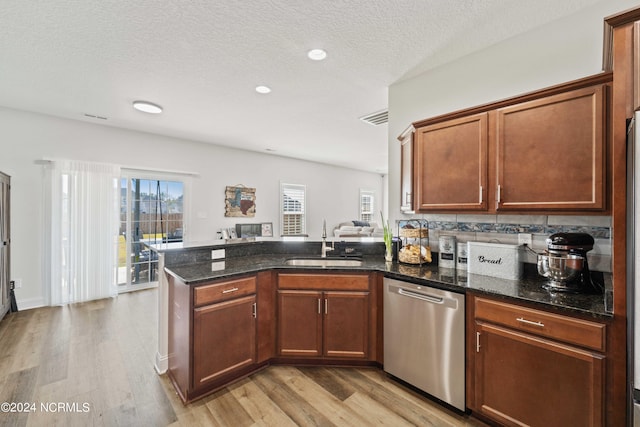 kitchen with sink, a textured ceiling, dishwasher, dark stone countertops, and light wood-type flooring