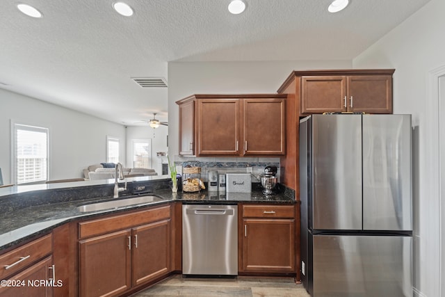 kitchen with light hardwood / wood-style floors, stainless steel appliances, ceiling fan, dark stone counters, and sink