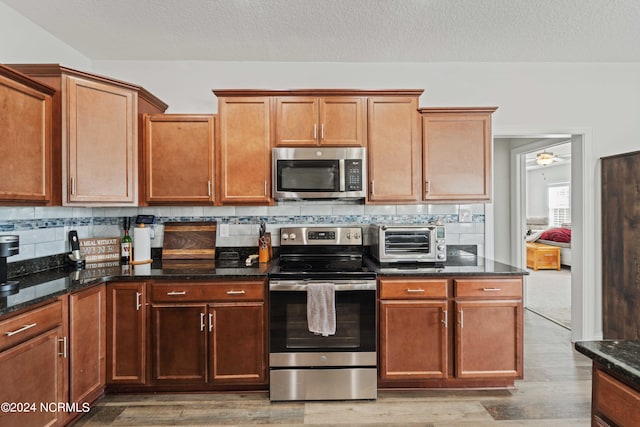 kitchen featuring backsplash, dark stone countertops, light hardwood / wood-style flooring, and stainless steel appliances