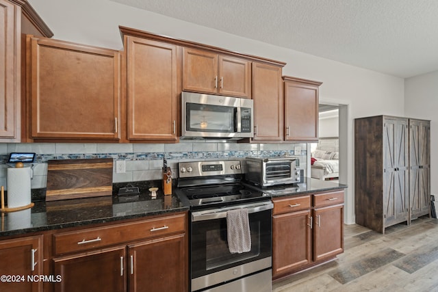 kitchen with stainless steel appliances, dark stone countertops, light hardwood / wood-style floors, and tasteful backsplash