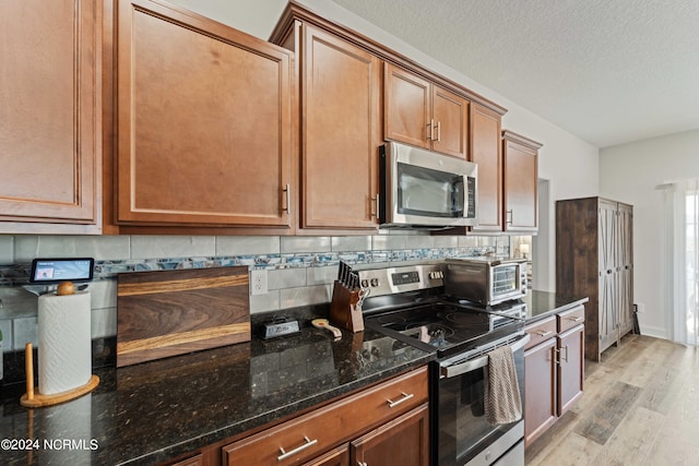 kitchen featuring light hardwood / wood-style flooring, dark stone countertops, decorative backsplash, and appliances with stainless steel finishes