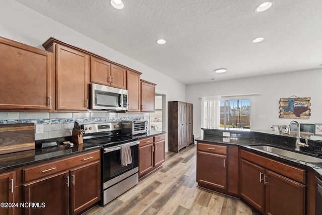 kitchen featuring dark stone countertops, stainless steel appliances, a textured ceiling, light hardwood / wood-style flooring, and sink