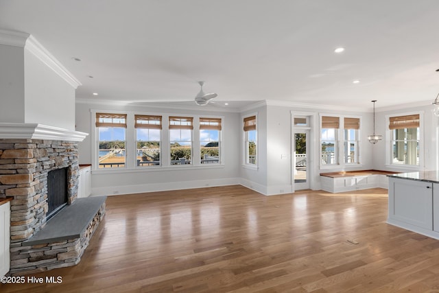 unfurnished living room with ornamental molding, ceiling fan with notable chandelier, a fireplace, and light hardwood / wood-style flooring