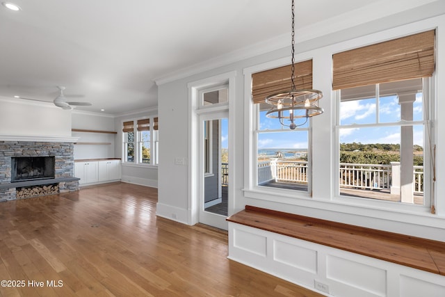 interior space featuring crown molding, wood-type flooring, a fireplace, and ceiling fan with notable chandelier