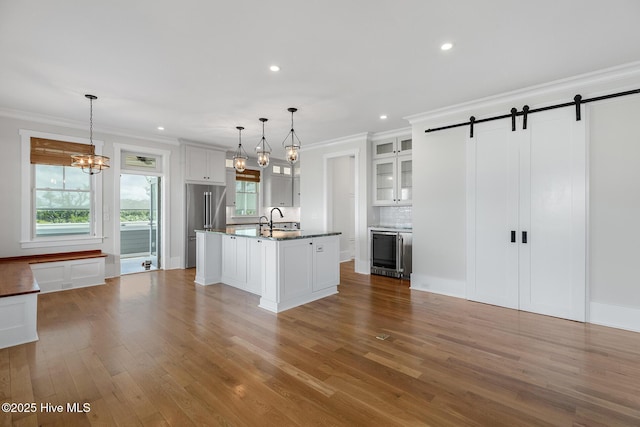 kitchen featuring white cabinetry, a barn door, decorative light fixtures, and a kitchen island with sink