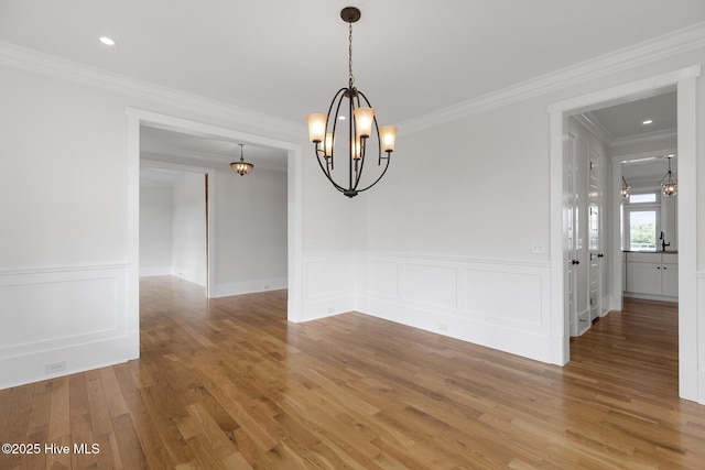 unfurnished dining area with sink, hardwood / wood-style flooring, ornamental molding, and a chandelier