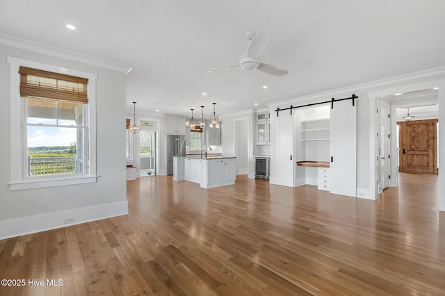 unfurnished living room featuring sink, crown molding, wood-type flooring, ceiling fan, and a barn door