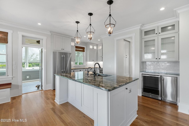 kitchen featuring high end fridge, sink, white cabinetry, decorative light fixtures, and an island with sink