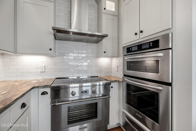 kitchen with appliances with stainless steel finishes, tasteful backsplash, white cabinets, dark stone counters, and wall chimney exhaust hood