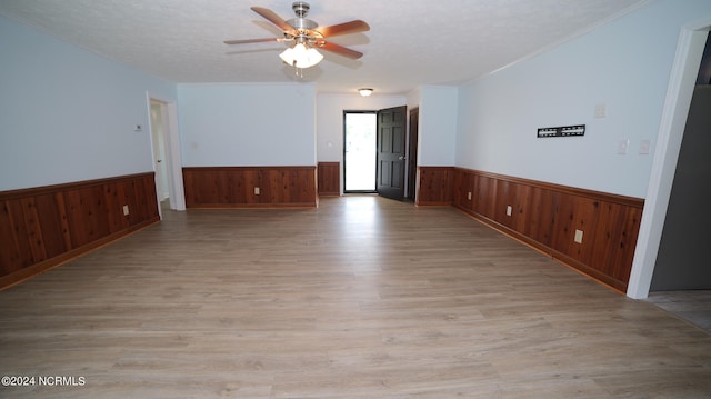 unfurnished room with ceiling fan, light wood-type flooring, and wood walls