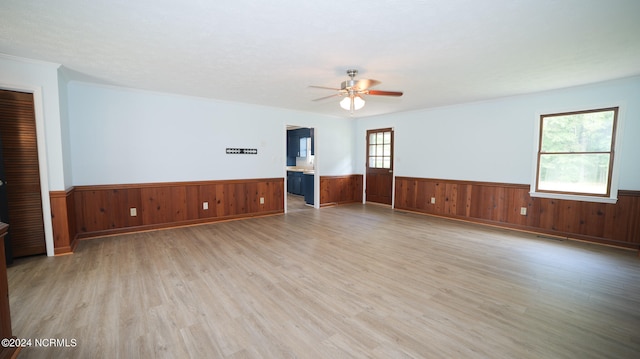 unfurnished room with crown molding, wood walls, ceiling fan, and light hardwood / wood-style flooring